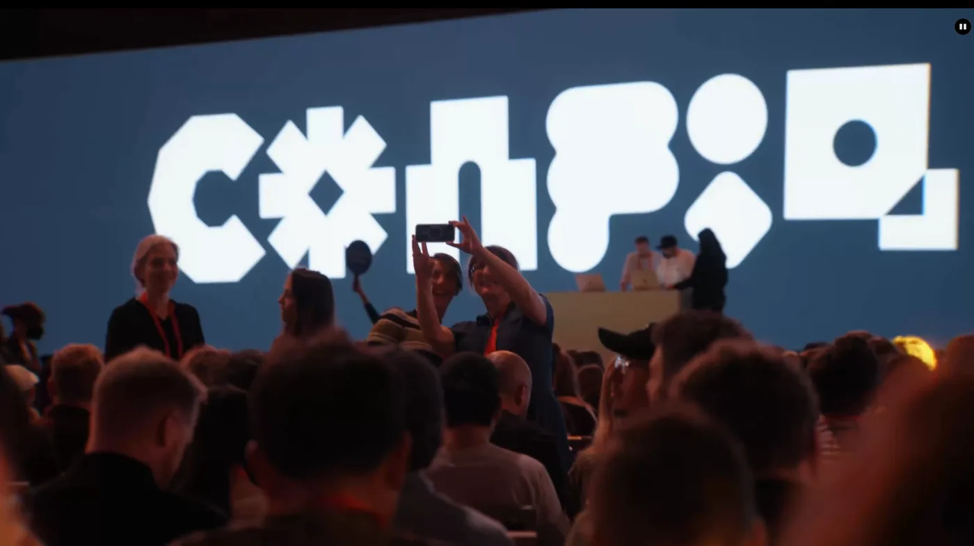 Conference attendees photograph the Figma Config logo projected on a large screen inside the main auditorium